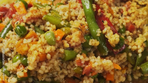 Stewed couscous with vegetables, green onion, carrots and tomatoes in milk rotates in a circle. Close-up.