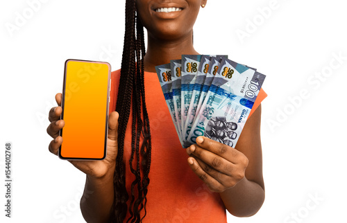 Beautiful Black woman lady smiling holding 100 Ghanaian cedi notes and showing pointing phone with blank screen to the camera over white background. Hand holding Ghanaian currency notes
