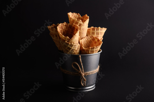 Waffle cones are neatly stacked in a metal bucket, showcasing their crunchy texture, perfect for holding ice cream or desserts