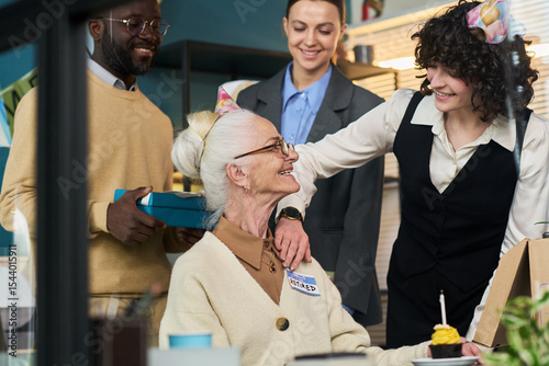 Fotografie Senior Caucasian woman sitting at desk wearing retired badge smiling at multieth
