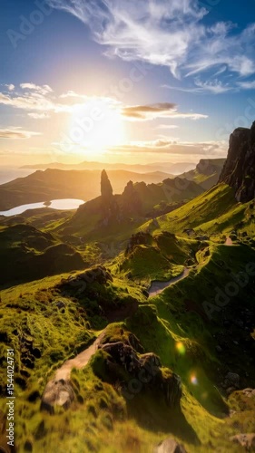 Scenic landscape with a dramatic rock formation, grassy hills, a meandering path, lake, and bright sun against a blue cloudy sky