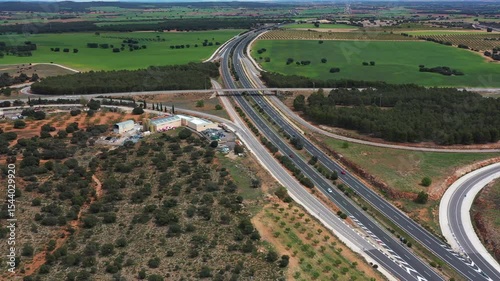 Aerial drone view of highway running through lush farmland with overpass, surrounding trees, and rural development showing modern transport and countryside