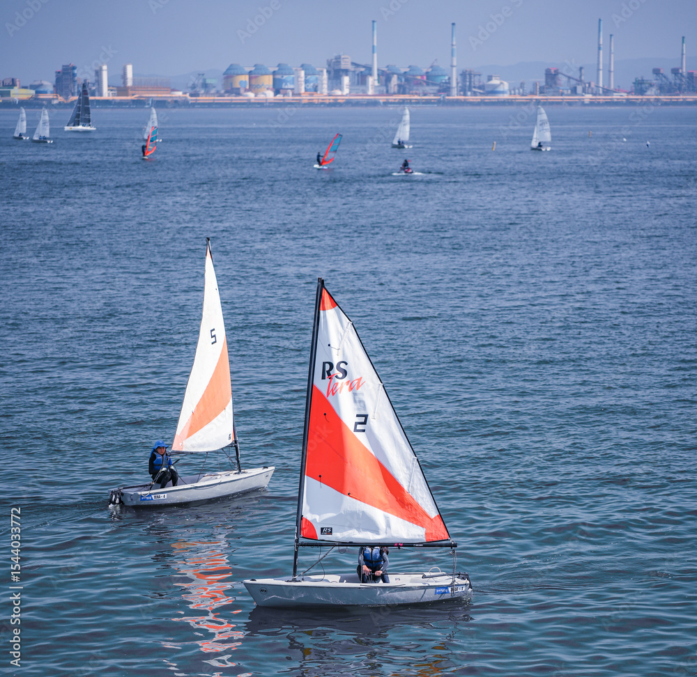 Fototapeta premium Pohang, Republic of Korea - July 02, 2023:Vibrant watersports scene in Pohang Bay. Dynamic watersports with sailboats and windsurfers.Sailboats, windsurfers and safety boats.