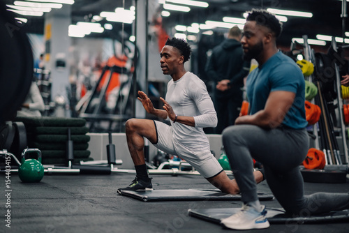 Εκτύπωση καμβά Two male athletes stretching legs on mats in gym