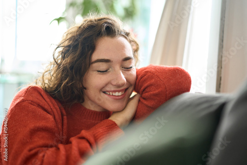 Young smiling pretty curly woman relaxing sitting on couch at home and chilling. Happy relaxed calm beautiful lady enjoying peace of mind and comfort of soft new sofa with eyes closed. Close up.
