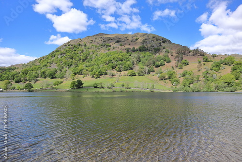 Panorama of Rydal Water with calm water and surrounding green hills under a partly cloudy blue sky. Lake District, England, UK. photo