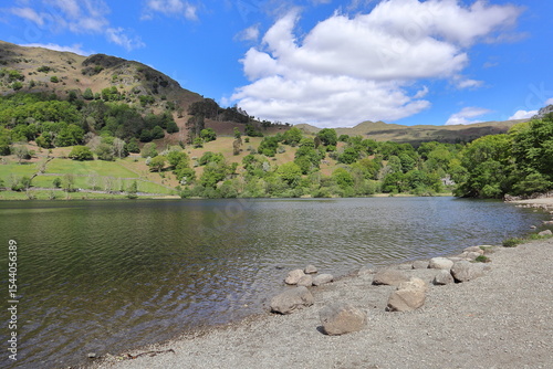 Shoreline of Rydal Water with rocks, calm water and surrounding hills under a partly cloudy sky. Lake District, England, United Kingdom. photo