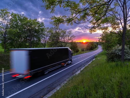 Motion blurred truck driving on asphalt road in rural landscape at sunset