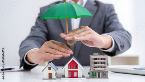 Man in Gray Suit Protecting Miniature Houses with Green Umbrella Real Estate Insurance Concept