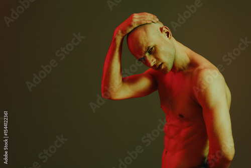 Strong man posing with a thoughtful expression, illuminated by dramatic red light against a dark background, creating a striking black and white image.