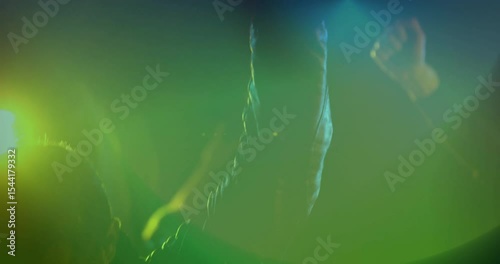 Fan lifting leather-sleeved arm and forming rock horns amid stage lights revealing music haze