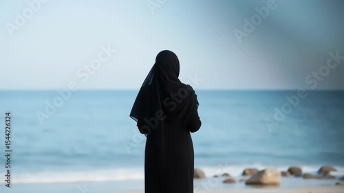 A contemplative muslim woman in hijab looking towards the ocean horizon