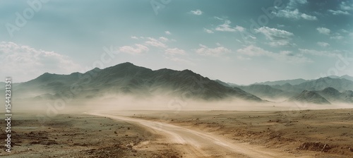 Vast panoramic desert landscape with distant mountains and a straight road leading to the horizon, featuring dust clouds, dry terrain, and atmospheric particles under a muted, cinematic tone