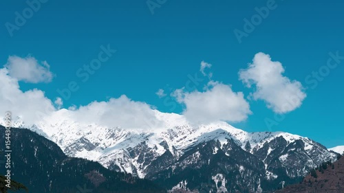 4K Time Lapse of Clouds moving above snowy Himalaya  during winter season as seen from Naggar, Himachal Pradesh, India. Sunny winter day with blue sky. Travel, nature and holidays background. 