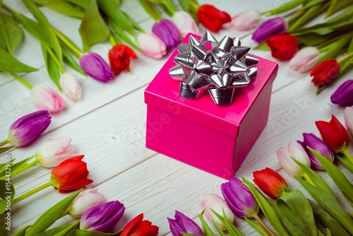 Fototapeta Naklejka Na Ścianę i Meble -  Flat-design pink gift box is resting on white wooden table with silver bow and tulip wreath