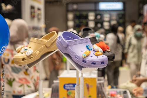 Colorful rubber clogs with decorative charms displayed on a store shelf, attracting shoppers in a crowded retail setting. Fun and playful footwear fashion in a modern shopping environme