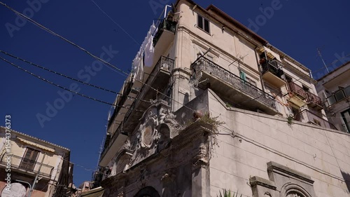 White laundry hanging from balconies of a residential building in Pizzo Calabro, a picturesque town in Southern Italy, under a vibrant blue sky