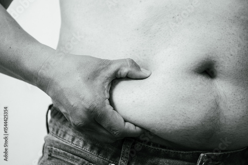 Obesity man body, fat male belly,close up on white background.A hand pinches the excessive fat on a person's stomach, highlighting issues of obesity or body weight.