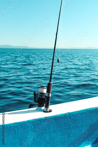 Fishing pole ready for action on a boat in the open sea with mountains behind