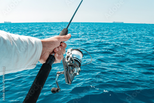 Hand holding a fishing rod with a spinning reel over the blue sea