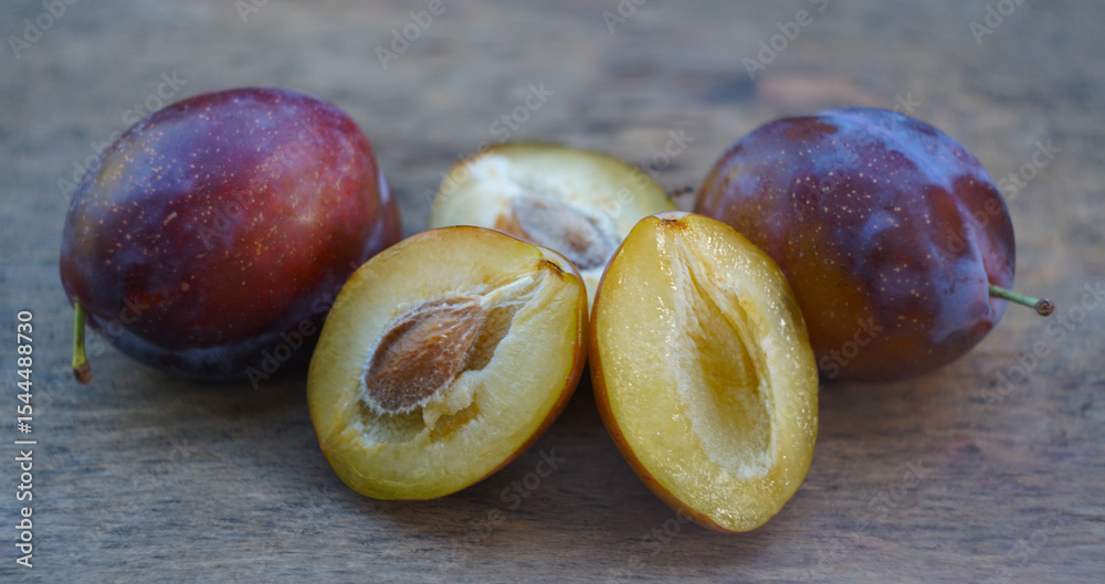 Fototapeta premium Cut and whole plums on a board in nature