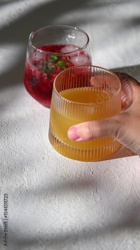 Hand take glass tumblers with red, yellow, and green lemonade. Cold summer drinks with ice and condensation drops on glass surface. Refreshing for hot weather and restaurant