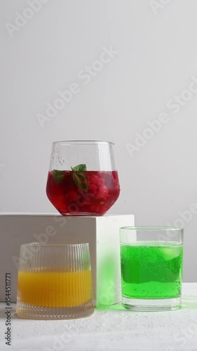 Three glass tumblers with red, yellow, and green lemonade on white background. Cold summer drinks with ice and condensation drops on glass surface. Refreshing for hot weather and restaurant