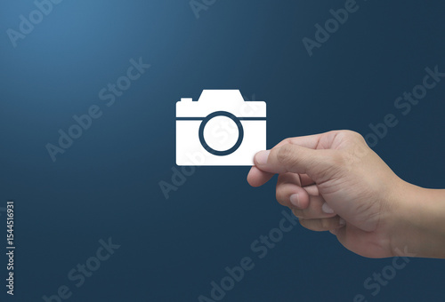 Hand holding camera flat icon in fingers over light blue background, Business camera service shop online concept