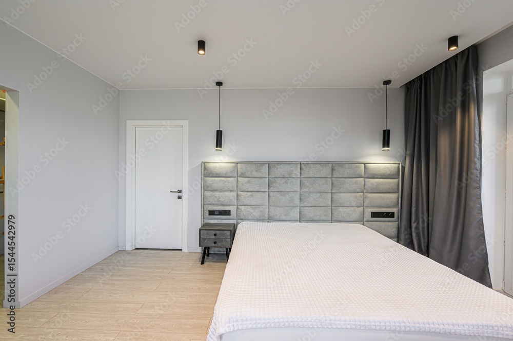 Fototapeta premium Modern bedroom featuring a bed with a gray headboard, white bedding, gray walls, and minimalist black lighting fixtures