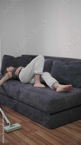 Exhausted woman collapsing onto the sofa in the living room after she vacuumed the floor. Household chores and clean lifestyle Cleaning concept