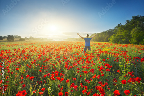 A man stands in a field of poppies and strive up arms to sun