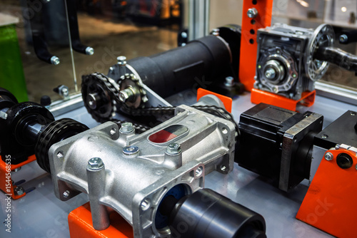 Close-up of various mechanical components: gears, chains, gearbox, and motor, used in automation and industrial machinery. Precision engineering parts on display.
