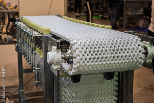 Close-up of a white modular plastic conveyor belt with yellow support rollers, part of an industrial manufacturing or assembly line.