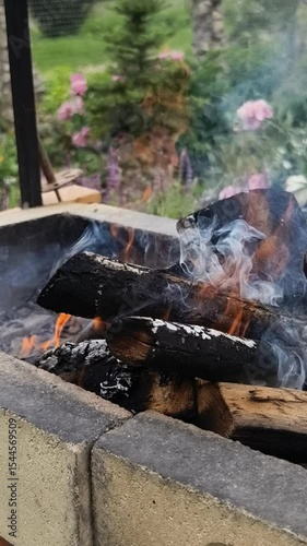 A close-up vertical video of firewood burning intensely in a stone barbecue grill, with thick smoke rising. Perfect for content about cooking, grilling, summer gatherings, or as a cozy atmospheric