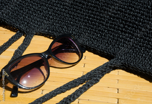 Lace black raffia bag and black sunglasses on a wooden mat.