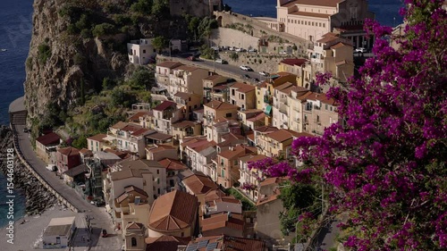 Purple bougainvillea blooming over the colorful houses of Scilla, Calabria, with the Sanctuary of Madonna di Reggio in the background