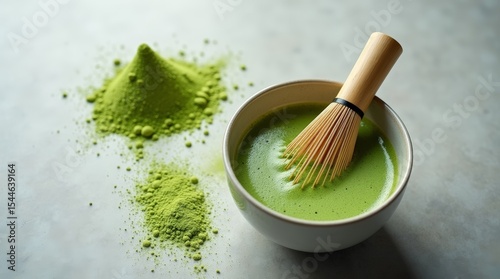 Freshly whisked matcha green tea in ceramic bowl with bamboo whisk and matcha powder on stone surface. Healthy organic drink