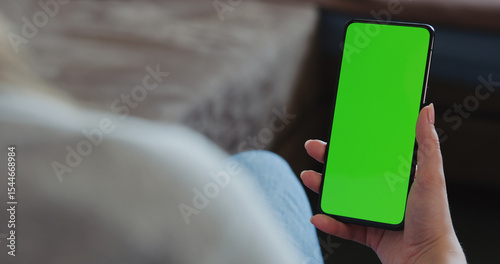 young woman sitting in a chair with smartphone with green screen