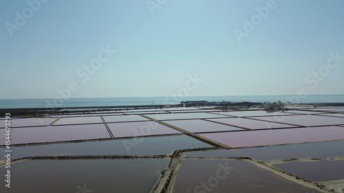 Geometric pink salt evaporation ponds beside the Mediterranean Sea with distant harbor buildings and horizon in San Pedro del Pinatar Murcia offering a coastal industrial and natural scenery for envir