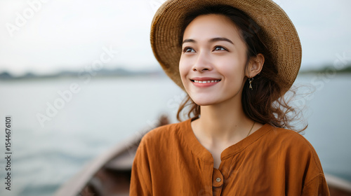 Fototapeta Naklejka Na Ścianę i Meble -  Joyful young woman tourist in Asian hat standing on boat at lake