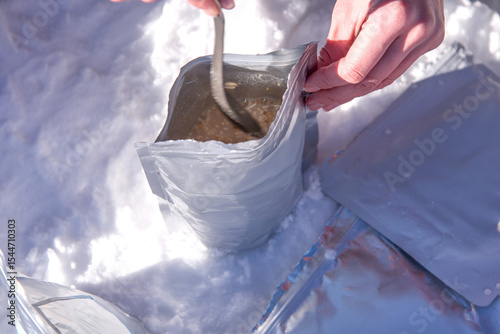 Hands preparing freeze-dried meal in pouch on snow. Close-up of dehydrated camping food during winter outdoor adventure
