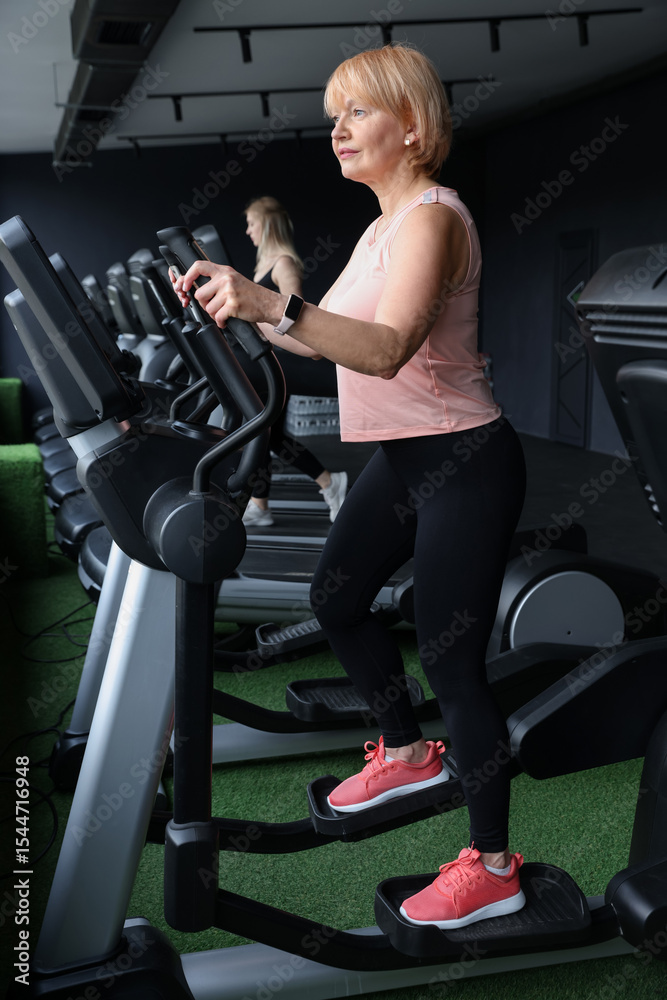 Fototapeta premium Senior woman training on elliptical machine in gym