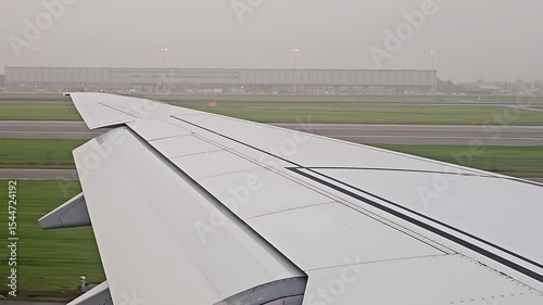 Airplane wing view with clear blue sky and landscape below, seen during flight.