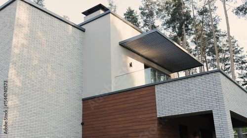 Modern architectural brick house with balcony. Two-story private house, elegantly surrounded by lush green trees and nature.