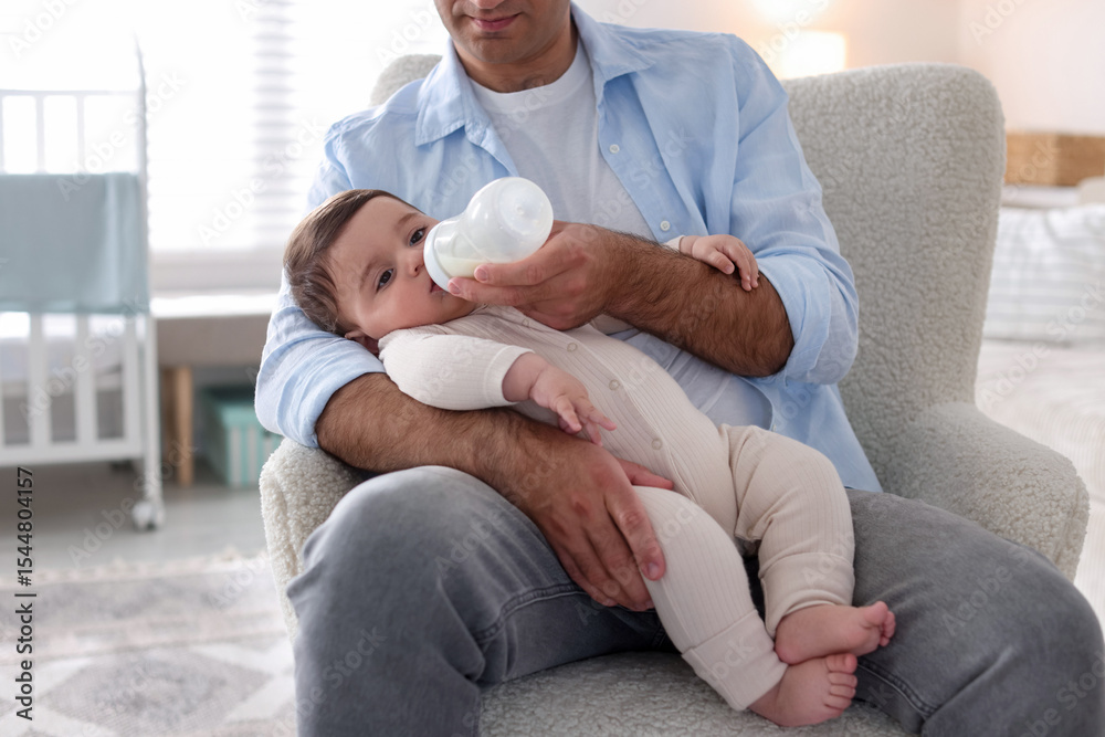 Fototapeta premium Father feeding his little baby with bottle on armchair at home, closeup