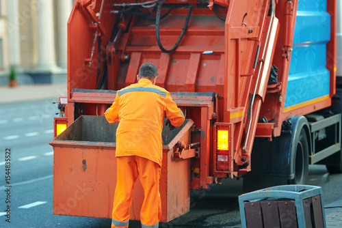 Φωτογραφία Worker in orange clothing disposes trash in garbage truck to maintain urban cleanliness