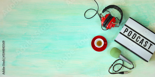 Top view  of podcast concept, lightbox with letters podcast on it, vintage headphones cup of coffee and professional microphone. Negative space technique with free copy space.
