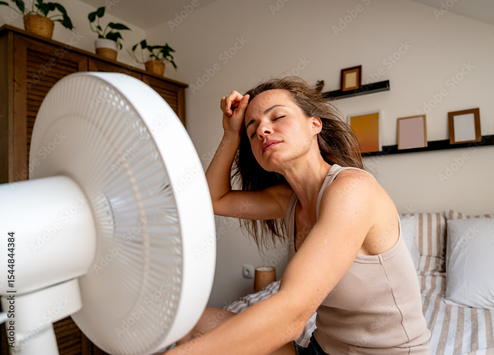 Overheated woman cooling off on bed with electric fan at home Overheated woman cooling off on bed with electric fan at home