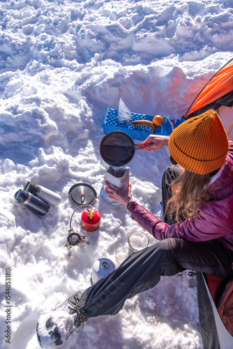 Woman pouring hot water into freeze-dried meal outside winter tent. Winter outdoor cooking during alpine expedition