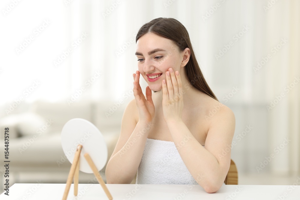 Smiling woman with healthy skin massaging face and round mirror at table indoors Smiling woman with healthy skin massaging face and round mirror at table indoors